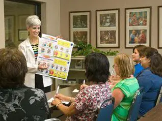 A woman is holding up a board while people sit around.