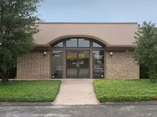 A building with grass around it and bushes in front of the door.